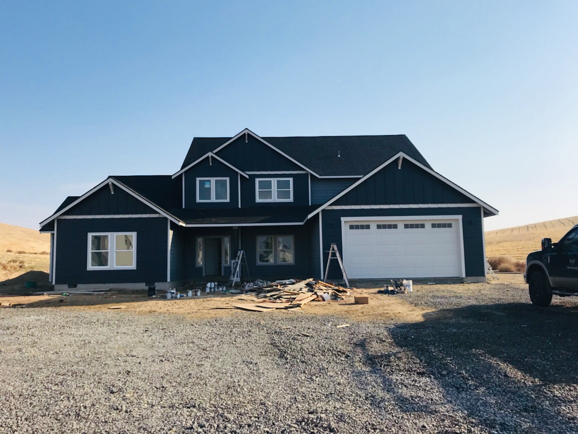 Two storey craftsman home finished in deep charcoal with white trim, Eastern Oregon hills behind