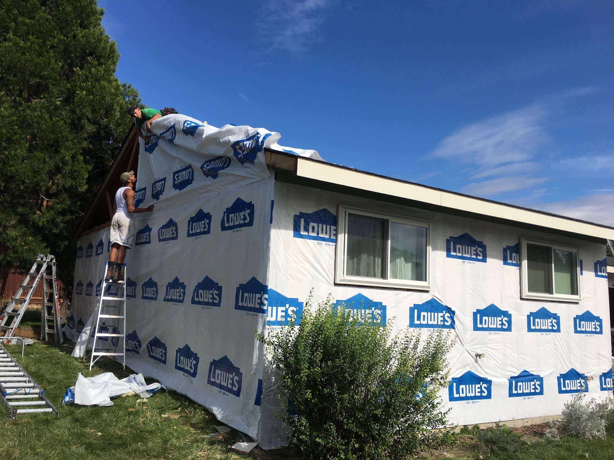 Two crew members on ladders masking a whole house in protective sheeting before painting