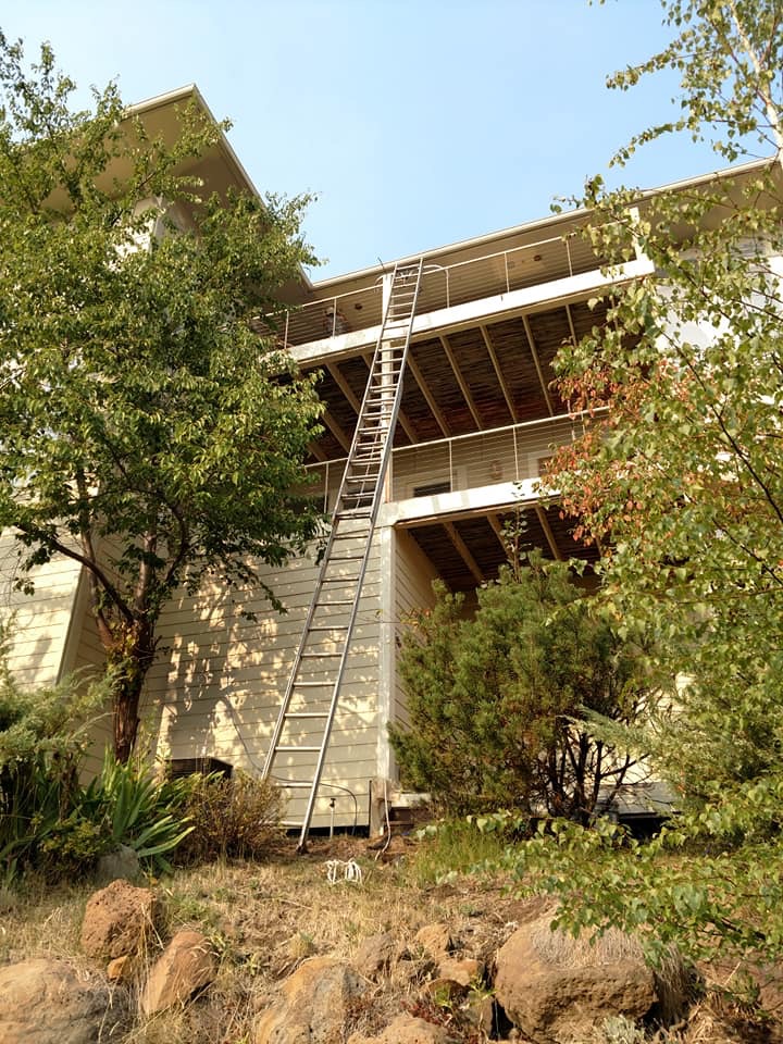 Extension ladder set against a two story cream colored house in the afternoon sun